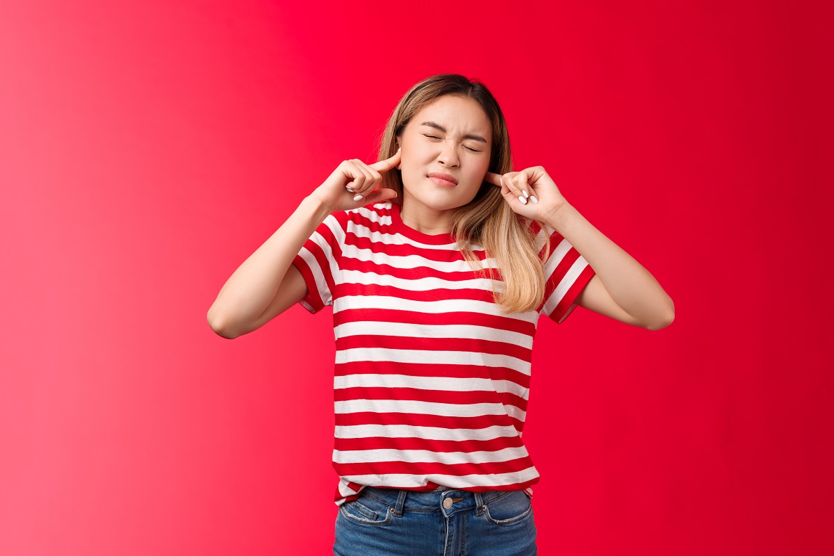 woman in a striped red shirt covering her ears, eyes shut